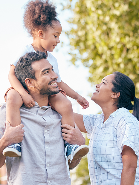 young family of three walking outside with child on dads shoulders.