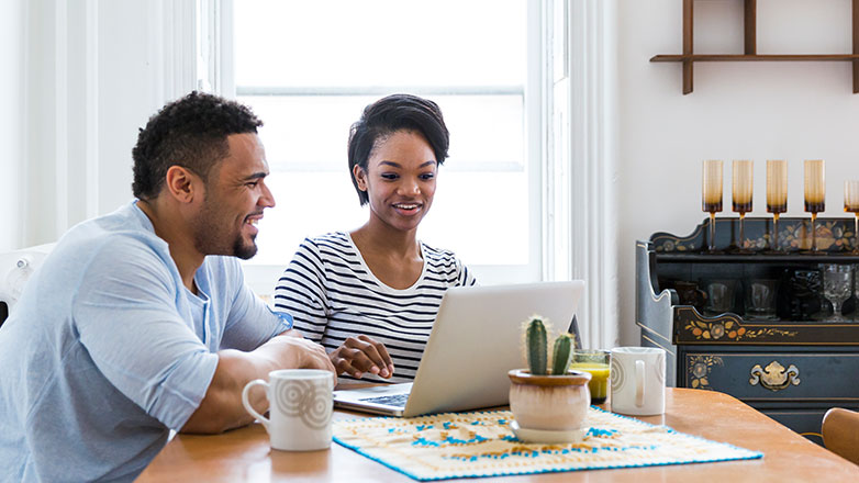 Couple sitting at their kitchen table looking at their laptop.