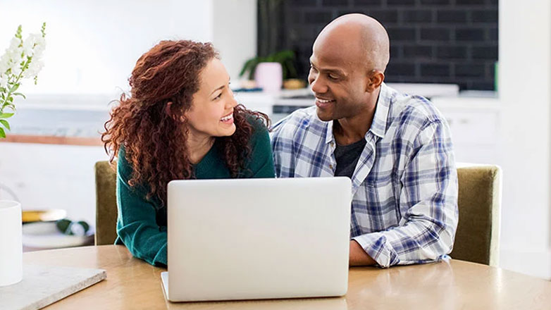 Husband and wife view a document on a laptop together in their home.