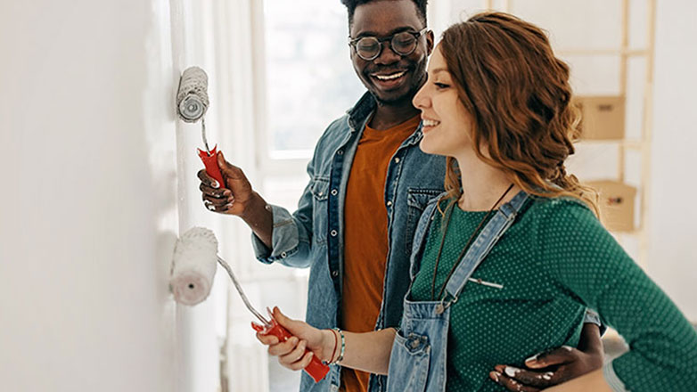 A young couple paints a wall in their new home together.