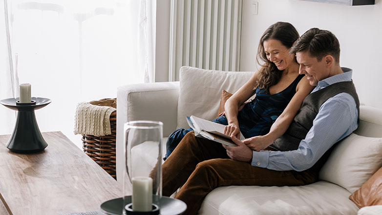 Couple sitting on couch together looking at a book.