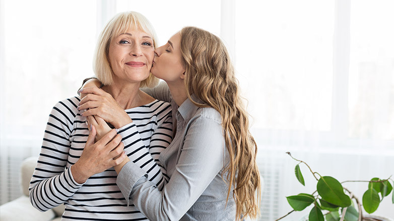 daughter hugging mom and kissing her on the cheek.