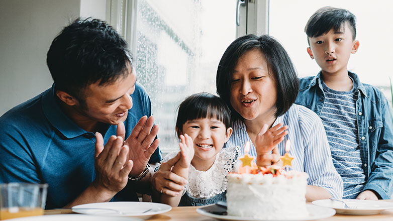 Parents sing happy birthday to their little girl as she happily claps and looks at her birthday cake.