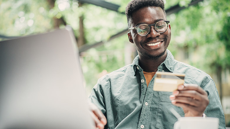 man looking at his credit card while online shopping on his laptop.