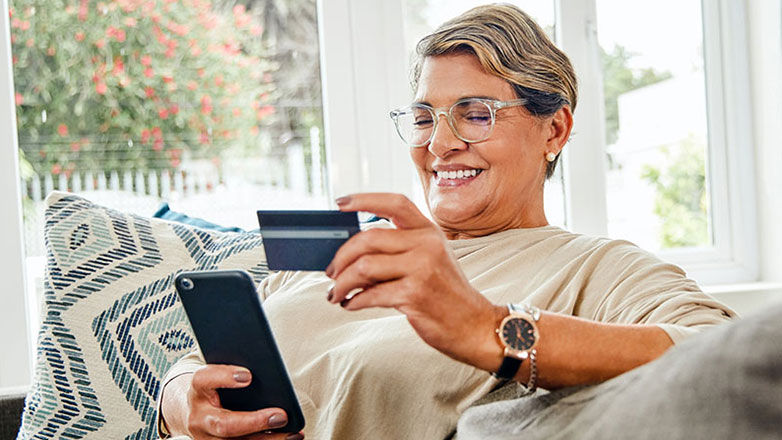 Mature woman making a purchase on her phone with her debit card.