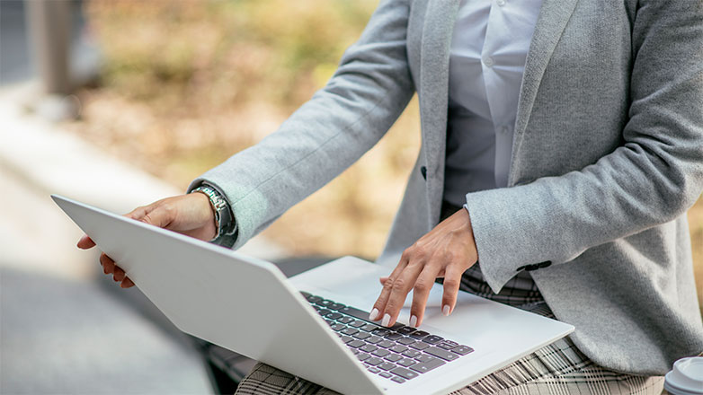 Woman sitting on a bench outside and working on her laptop.