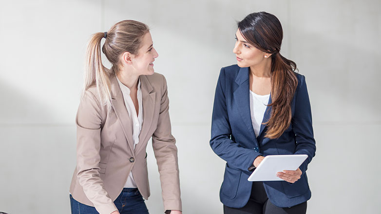 Two professional females standing at a desk talking to each other.