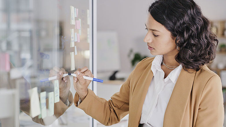 Young professional takes notes from a meeting on a board.