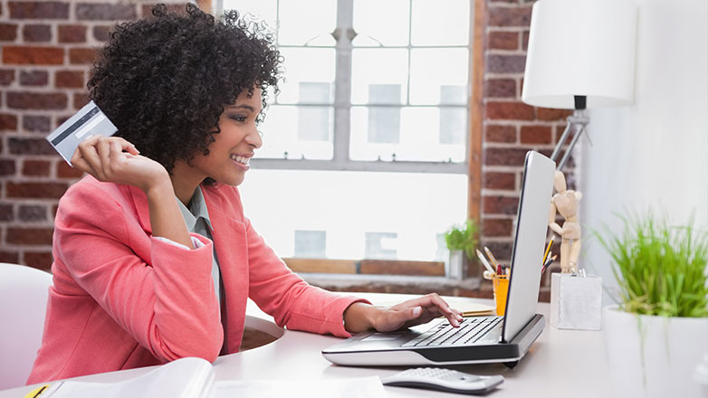 business woman smiling at computer holding credit card