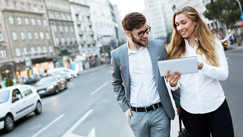 man and woman walking down street looking at tablet