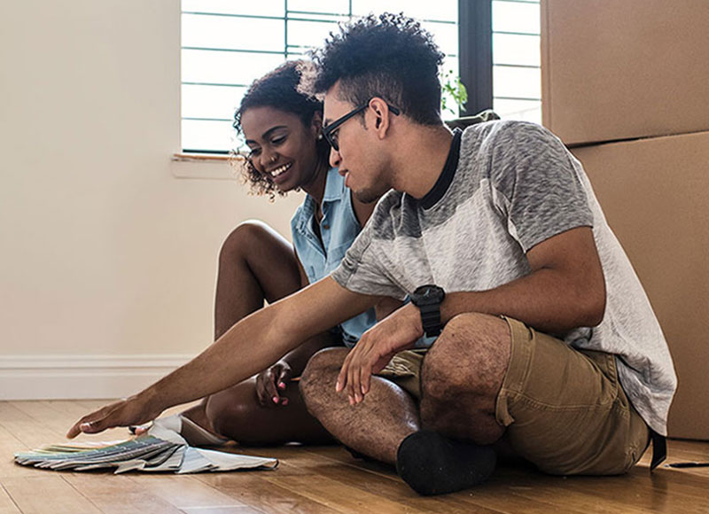 Young couple picking out paint swatches while sitting on the floor of their new home.