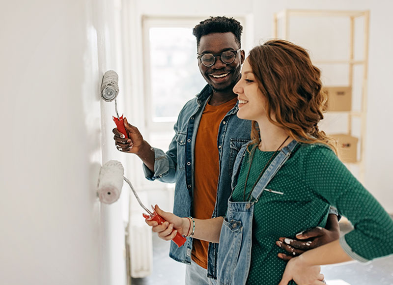 A young couple paints a wall in their new home together.