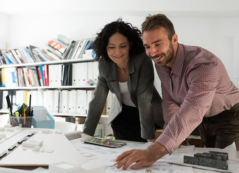 Two work colleagues review papers together on a work desk.