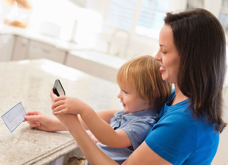 Mom sitting with baby in her lap and depositing a check with her phone.