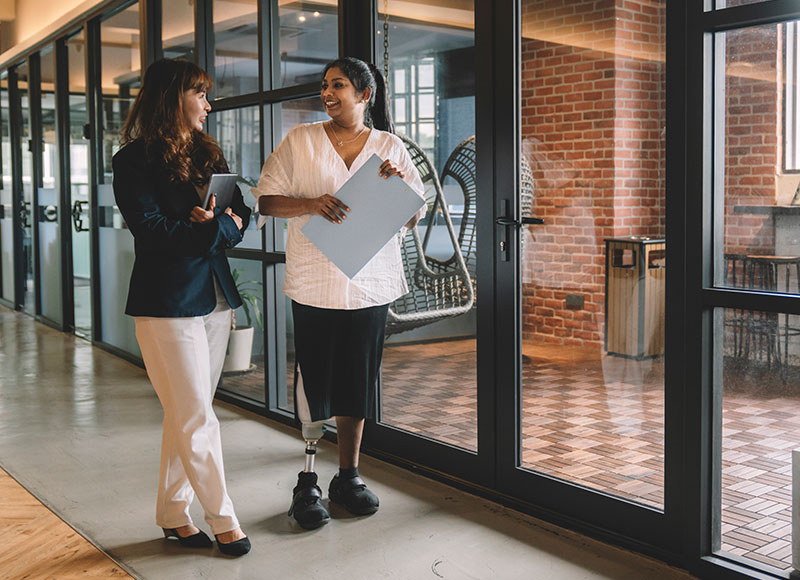 Work colleagues walk down the hallway of their workpace together.