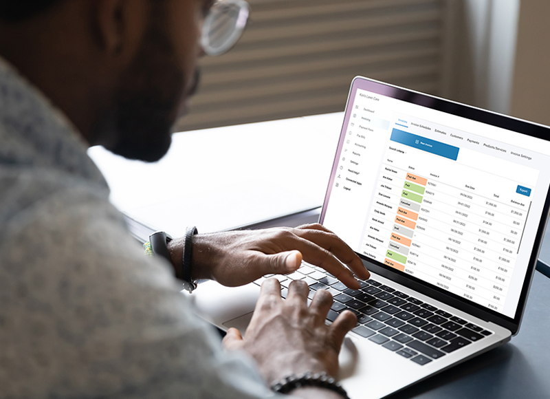 A person is using a laptop computer. He is looking at a screen with a table of data. He is wearing glasses and has a watch on his left hand.