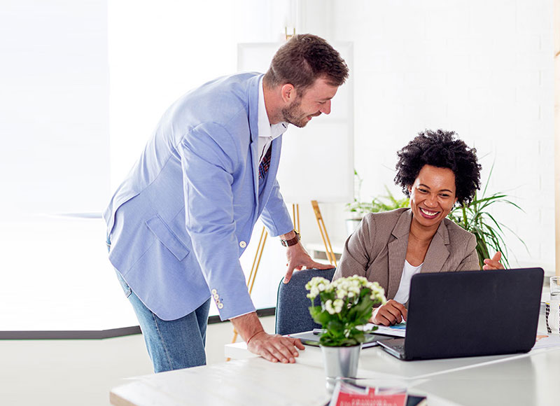 Woman working at her desk and showing her colleague a document on her laptop.