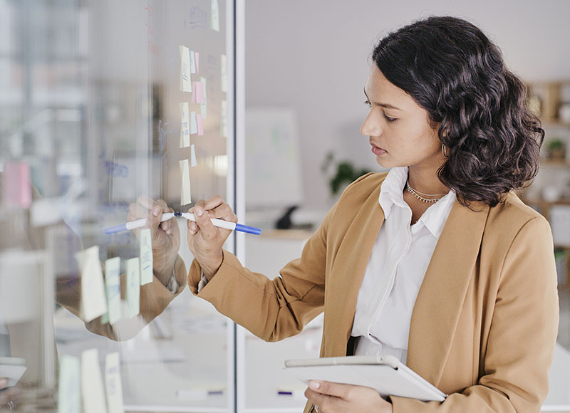 Young professional takes notes from a meeting on a board.