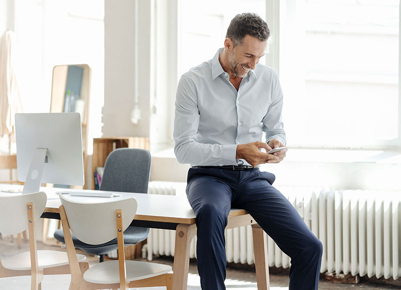 Man standing next to his desk looking at his mobile phone.