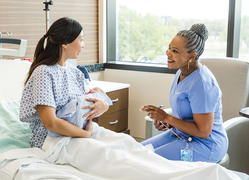 Nurse happily checks in with a new mother at her bedside in the hospital.